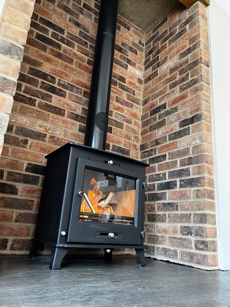 Modern black wood-burning stove with visible flame installed in exposed brick fireplace